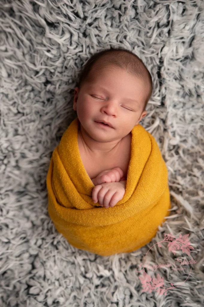 Nouveau-né emmailloté dans un tissu jaune lors de sa séance en studio